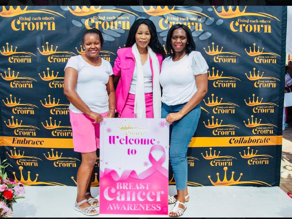 Three women at an FEOC Breast Cancer Awareness Day photo backdrop holding a welcome sign