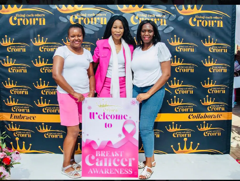 Three women at an FEOC Breast Cancer Awareness Day photo backdrop holding a welcome sign